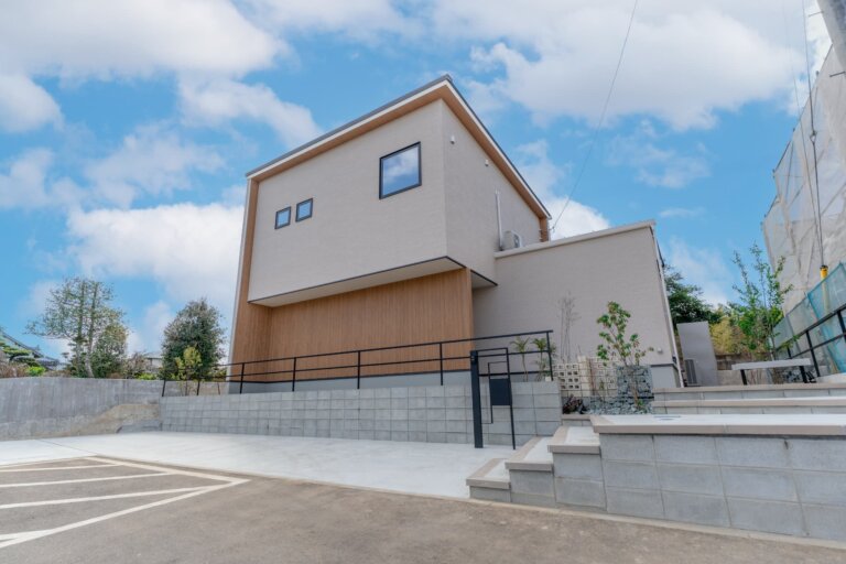 やわらかなグレーと木目が調和し、片流れ屋根のすっきり感が心地よい二階建てに見えます。